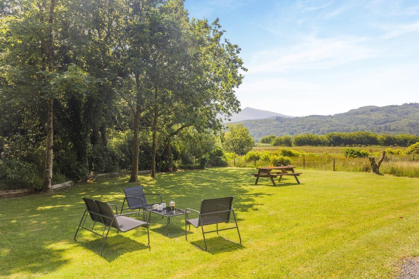 Een buitenruimte met een picknicktafel en stoelen, omgeven door weelderige begroeiing en uitzicht op glooiende heuvels.