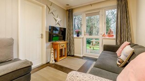 Ein Wohnzimmer mit einer Couch, einem Fernseher, einem kleinen Tisch und einem Fenster mit Vorhängen.