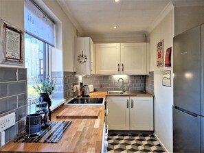 A modern kitchen with white cabinets, a stainless steel refrigerator, a black and white checkered floor, and a window with a view of the outdoors. - 2 Bed in Penzance (oc-m27232) (Gulval)