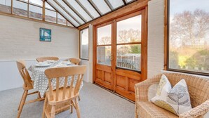 Une pièce avec une table dressée pour le repas, une chaise en osier avec des coussins, une porte en bois et une grande fenêtre.