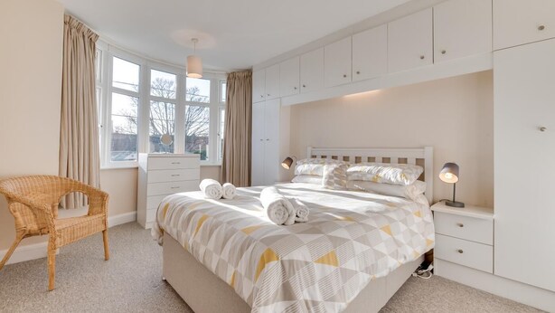 Une chambre à coucher avec un lit, des tables de chevet, une commode, une chaise et une fenêtre avec des rideaux.