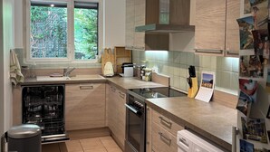 Een moderne keuken met een vaatwasser, oven en wasmachine, houten kastjes en een raam met uitzicht op groen.