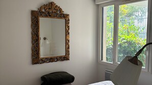 Een slaapkamer met een bed, een grote spiegel, een raam met uitzicht op groen en een bedlamp.