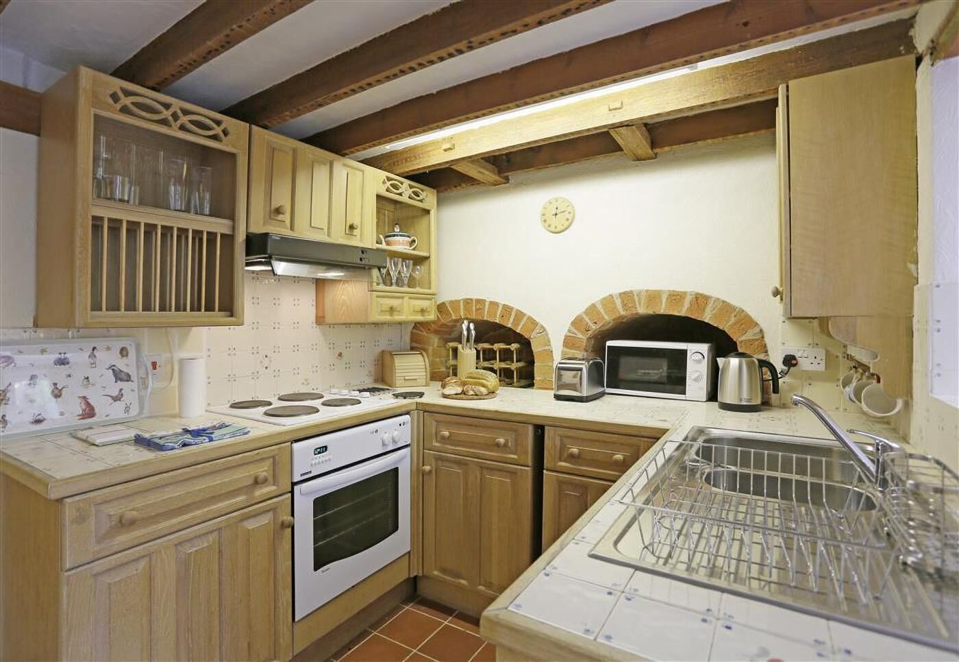 Een keuken met houten kasten, een fornuis, een magnetron en een bakoven.
