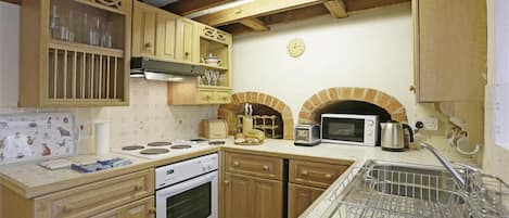Een keuken met houten kasten, een fornuis, een magnetron en een bakoven.