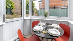A conservatory with a table set for four, red chairs, and a view of a brick building. - 2 Bed in Padstow (oc-p00557) (Padstow)