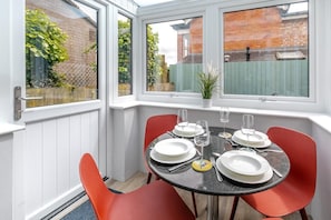 A conservatory with a table set for four, red chairs, and a view of a brick building. - 2 Bed in Padstow (oc-p00557) (Padstow)