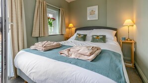 A double bed with two pillows, a window with curtains, a bedside lamp, and a flower wall art. - 2 Bed in Padstow (oc-p00557) (Padstow)