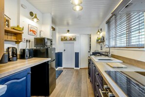 Eine moderne Küche mit Mikrowelle, Toaster und Kaffeemaschine auf der Arbeitsfläche, einem Spülbecken und einem Fenster mit Jalousien.