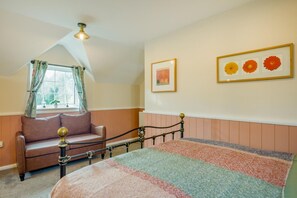 Ein Schlafzimmer mit einem Bett, einem Fenster mit Vorhängen, einer Couch und Wandbildern.