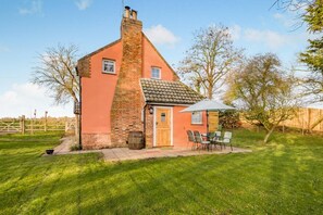 A single-story house with a brick chimney, a wooden door, and a small patio with a table and chairs. - 2 Bed in Wickhampton (oc-t34449) (Wickhampton)