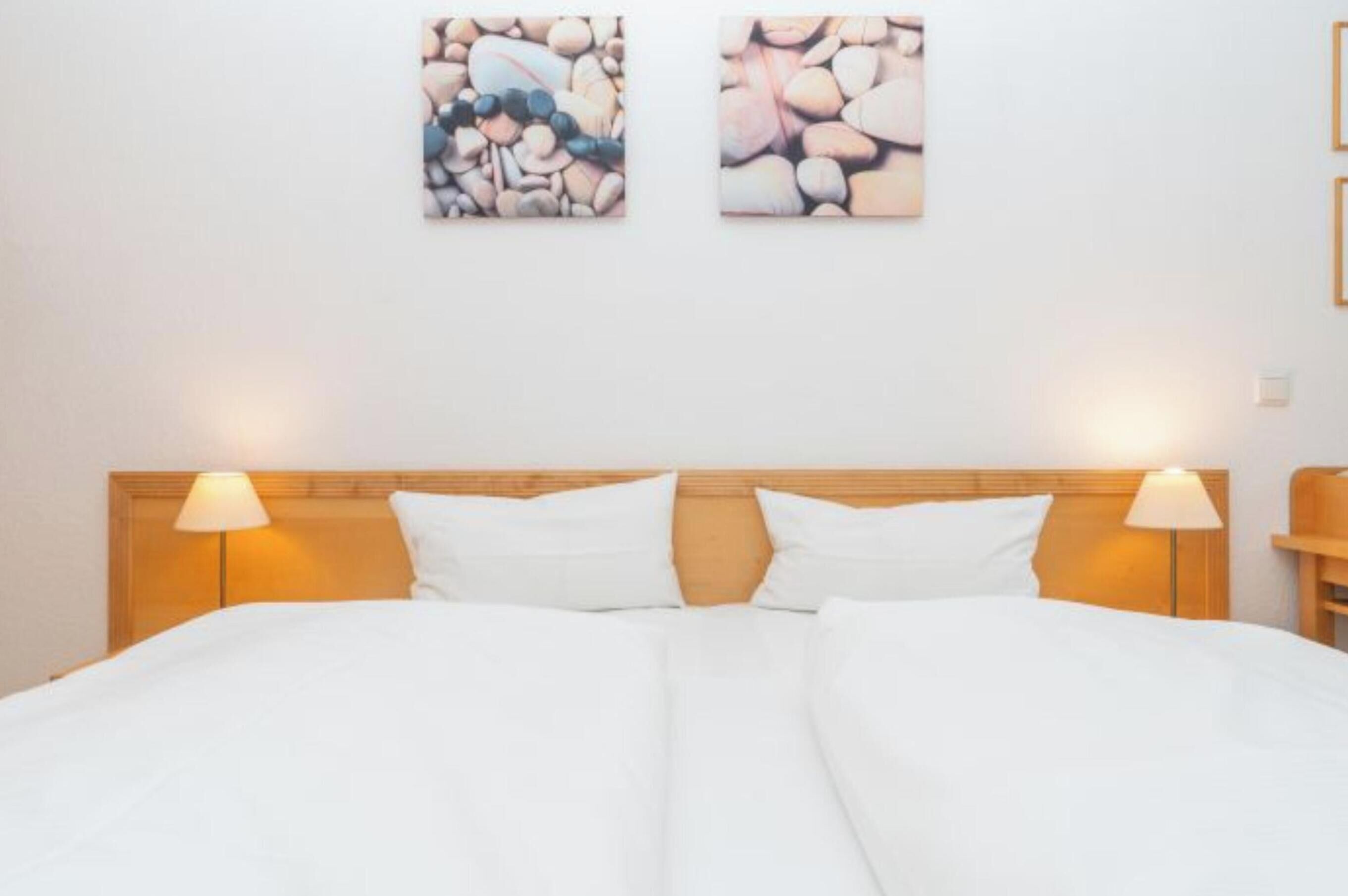 Un lit double avec une literie blanche, deux lampes fixées au mur et deux œuvres d’art abstraites au-dessus du lit.