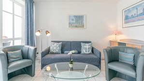 Una sala de estar moderna con un sofá, dos sillones, una mesa de centro de vidrio y una lámpara.