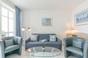 Ein stilvolles Wohnzimmer mit einer Couch, zwei Sesseln, einem Glastisch und einer Lampe.