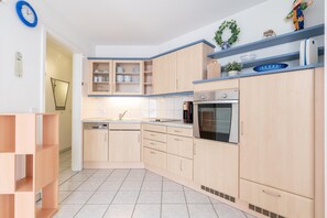 A kitchen with wooden cabinets, a dishwasher, an oven, and a clock on the wall. - Moderne Ferienwohnung Nahe Strand (Sellin)
