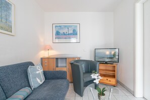 A modern living room with a sofa, a chair, a TV, a cabinet, and a framed picture on the wall. - Moderne Ferienwohnung Nahe Strand (Sellin)
