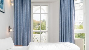 Un dormitorio con cama, ventana con cortinas y vistas a zonas verdes, además de un radiador blanco.