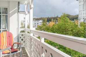 A balcony with a white railing, a chair, and a view of trees and buildings. - Moderne Ferienwohnung Nahe Strand (Sellin)