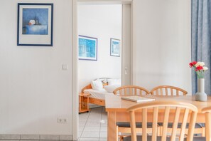 Ein Zimmer mit einem Bett, einem Esstisch mit Stühlen, einer Vase mit Blumen und gerahmten Bildern an der Wand.