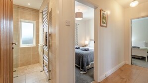 Ein Hotelzimmer mit Dusche, einem Bett mit grauer Bettdecke, einer Nachttischlampe und einem gerahmten Bild an der Wand.