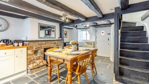 A rustic kitchen with a stone fireplace, wooden dining table, and a black staircase. - 1 Bed in Looe (oc-l30002) (Looe)