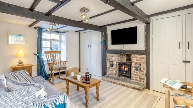 A room with exposed wooden beams, a fireplace, a sofa, a table with a cup and saucer, and a television mounted above the fireplace. - 1 Bed in Looe (oc-l30002) (Looe)