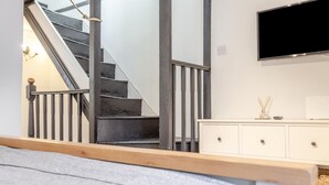 A bedroom with a bed, a white dresser, a TV mounted on the wall, and a staircase with a glass railing. - 1 Bed in Looe (oc-l30002) (Looe)