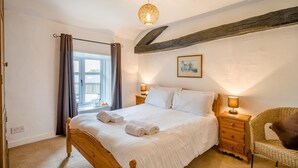 A bedroom with a wooden bed, bedside lamps, a wicker chair, and a window with curtains. - 2 Bed in Ings (oc-s34594) (Ings)