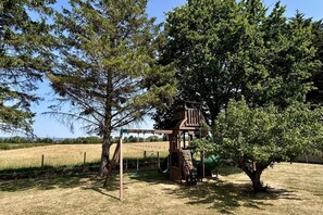 Ein Spielplatz mit einer hölzernen Kletterkonstruktion, Schaukeln und einer Rutsche.