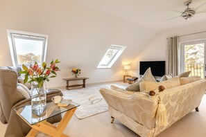 Ein geräumiges Wohnzimmer mit einer Couch, einem Glastisch, einem Fernseher und einem Deckenventilator.