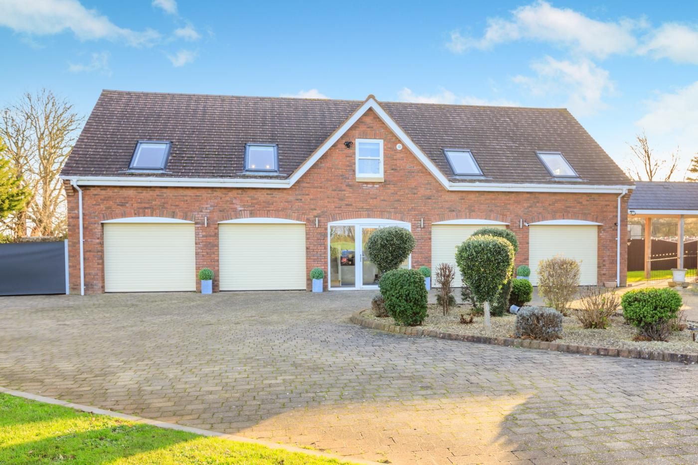 Een tweelaags bakstenen huis met een verharde oprit, drie garage deuren en een kleine tuin met vorm gesnoeide struiken.