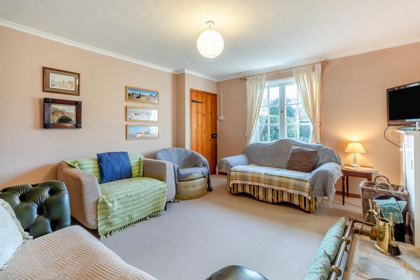 A living room with a sofa, armchairs, a television, and a window with curtains.