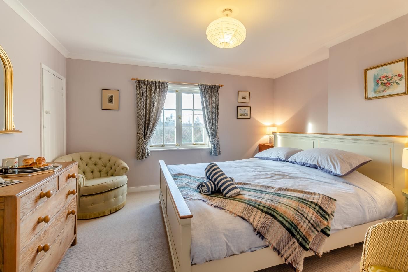 A bedroom with a bed, dresser, chair, window, and artwork.