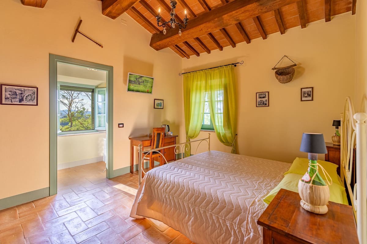 Un dormitorio con cama, escritorio, silla, lámpara y ventana con cortinas.