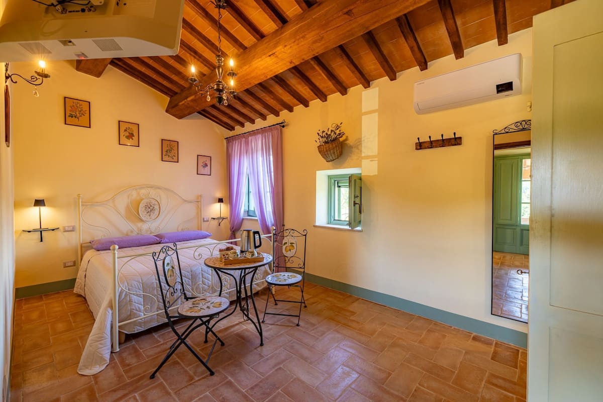 Un dormitorio con una cama, una mesa con sillas, una araña y una ventana con cortinas.