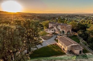 Vista aerea di un edificio rustico in pietra con un cortile, circondato da alberi e un paesaggio collinare.