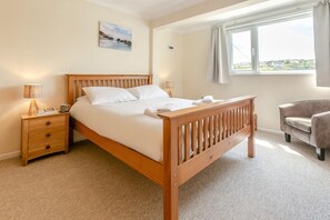Ein Schlafzimmer mit einem hölzernen Bett, einem Nachttisch, einem Stuhl und einem Fenster mit Vorhängen.