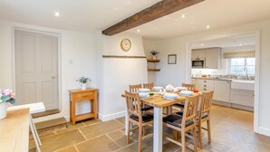 A dining area with a wooden table and chairs, a clock on the wall, and a kitchen in the background. - 3 Bed in Cundall (oc-l34088) (Cundall)