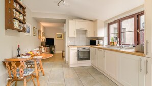A modern kitchen with white cabinets, a wooden dining table, and a built-in oven. - 1 Bed in Porthcawl (oc-94806) (Porthcawl)