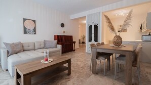 A living room with a sofa, coffee table, dining table, and chairs. There is a piano and a cabinet in the background. - Lora House by RentalsPro - Nea Moudania (Nea Moudania)