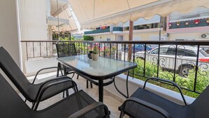 A balcony with a table and chairs, a railing, and a view of parked cars and greenery. - Lora House by RentalsPro - Nea Moudania (Nea Moudania)
