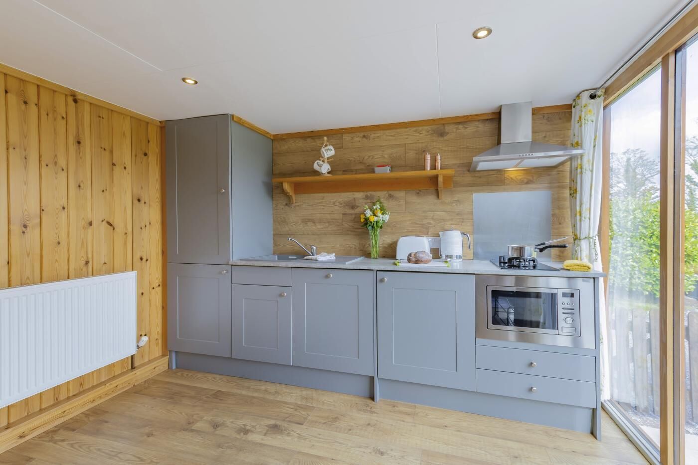 Une cuisine moderne avec des meubles gris, un four encastré et une fenêtre donnant sur un espace verdoyant.