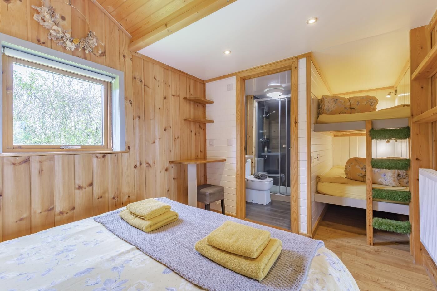 A wooden cabin with a bed, a bathroom, and a bunk bed.