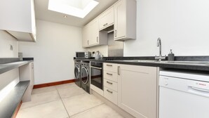 A compact kitchen with a dishwasher, washing machine, oven, microwave, and a skylight. - 3 Bed in Abersoch (oc-25959) (Llangian)