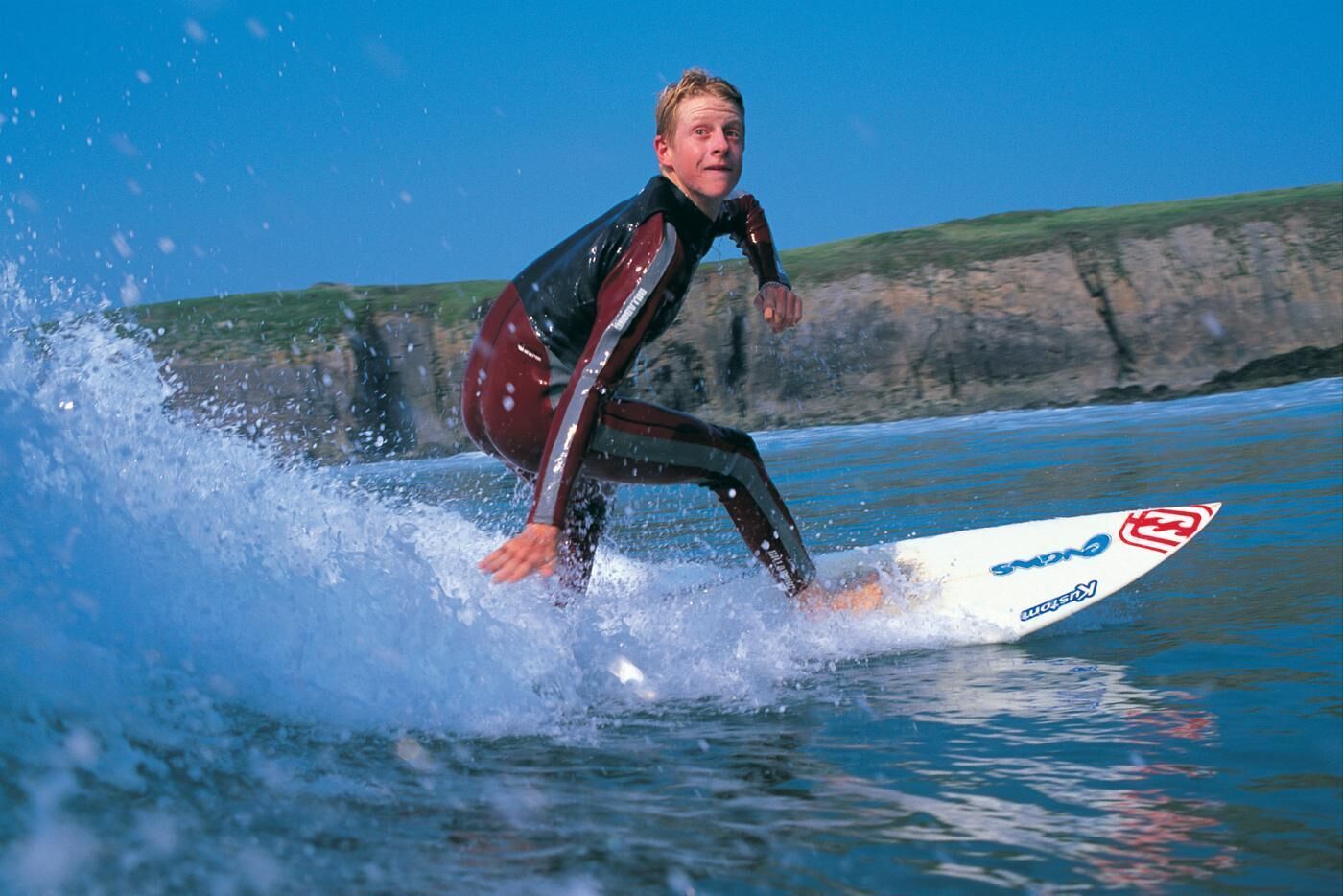 A person surfing on a wave with a surfboard that has a logo and text.