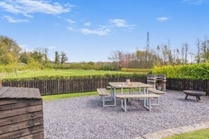 Un espace extérieur aménagé en terrasse, avec une table et des bancs, entouré d’une surface en gravier et d’une clôture en bois.