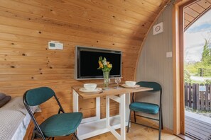Une pièce confortable avec un plafond en bois, une télévision, une petite table ornée d’un vase de fleurs, deux chaises et un lit.