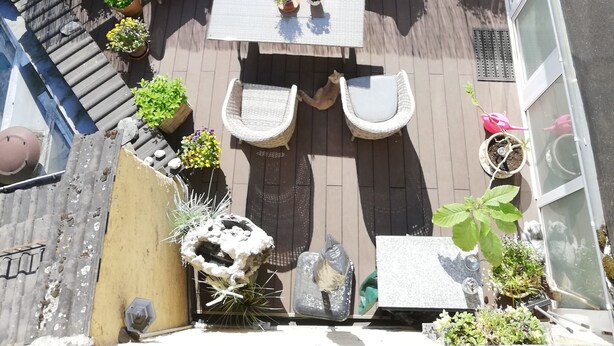 Um pátio externo com mesa e cadeiras, rodeado por plantas em vasos e um cercado de madeira.