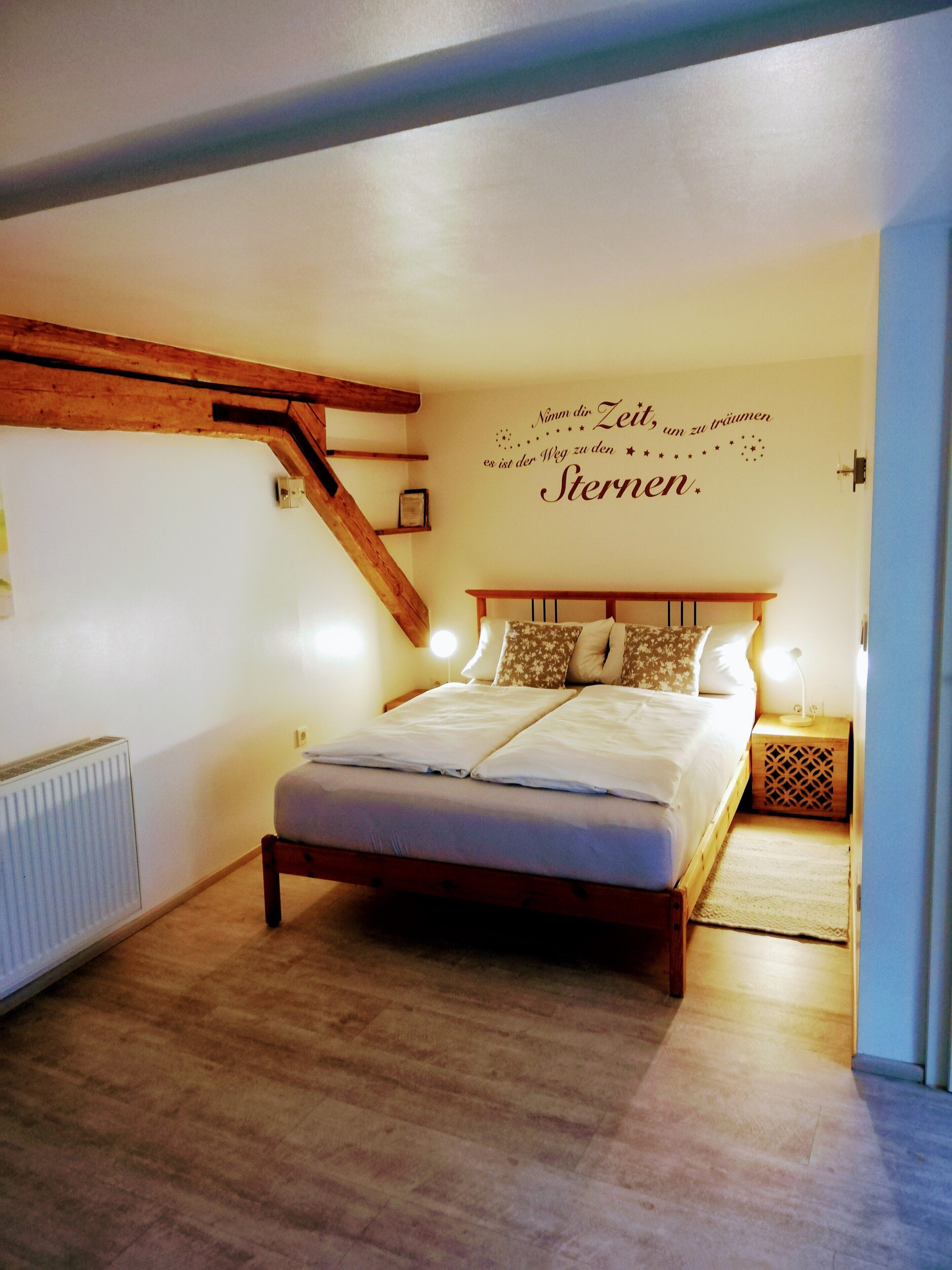 A bedroom with a wooden bed, a wall-mounted light, and a radiator.