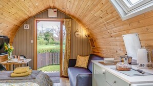 Ein gemütliches Holzhäuschen im Inneren mit Essbereich, einer Couch, einer Küchenzeile und Blick ins Freie.